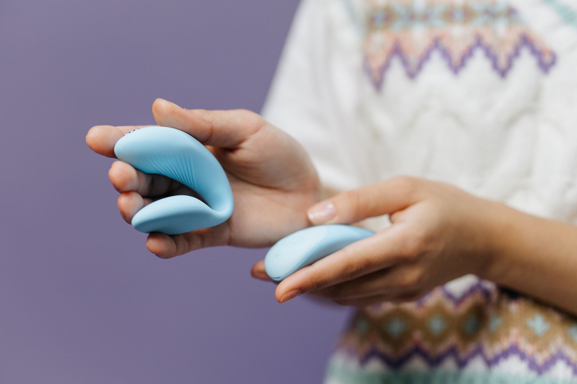 Close-up of hands holding a sleek blue lemon clitoral vibrator against a purple background.