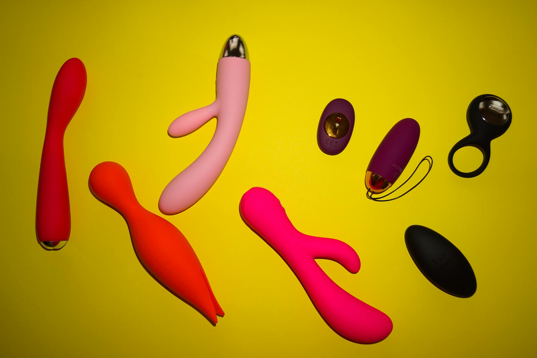 Colorful vibrators arranged on a bright yellow surface, showcasing variety in design and style